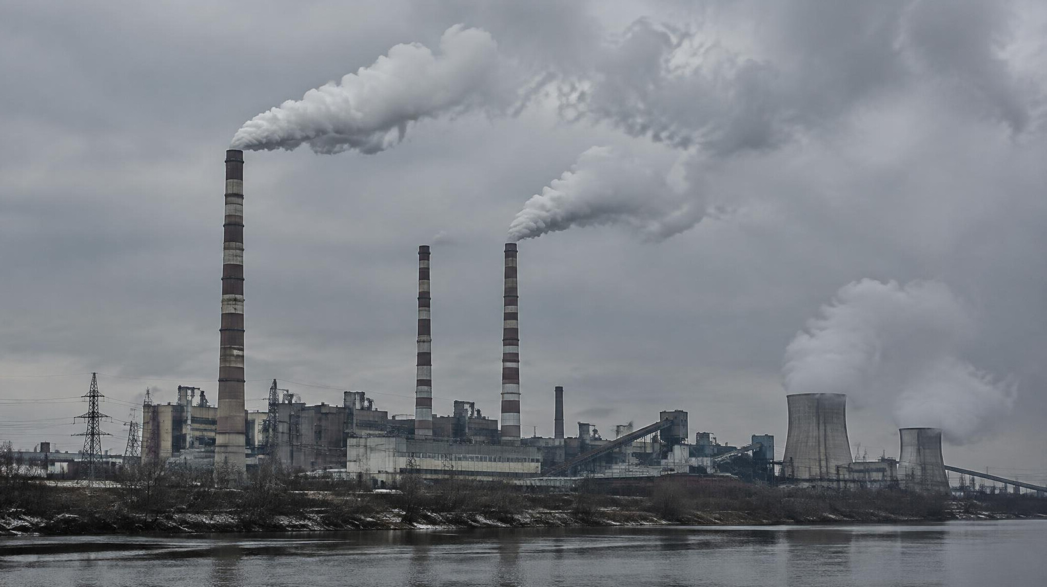 Industrial facility with tall smokestacks emitting smoke against a grey sky